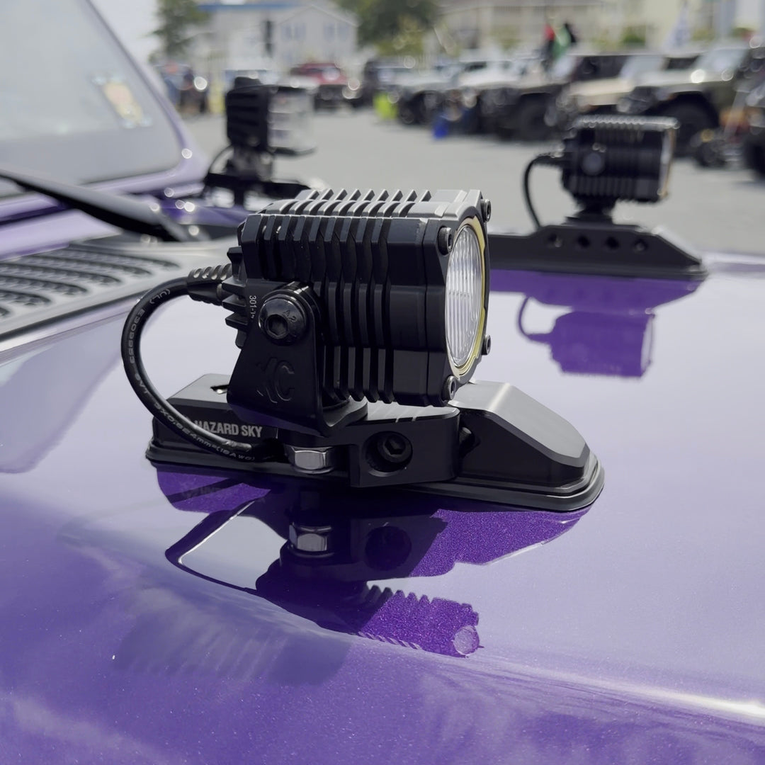 LED pod lights mounted on HazardKey billet hood bumpers with wiring routed through the passthrough on a purple Jeep Wrangler JL