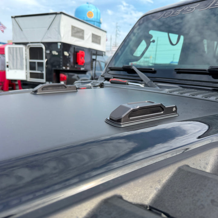 Pair of black billet aluminum hood bumpers installed on the gray hood of a Jeep Wrangler JL